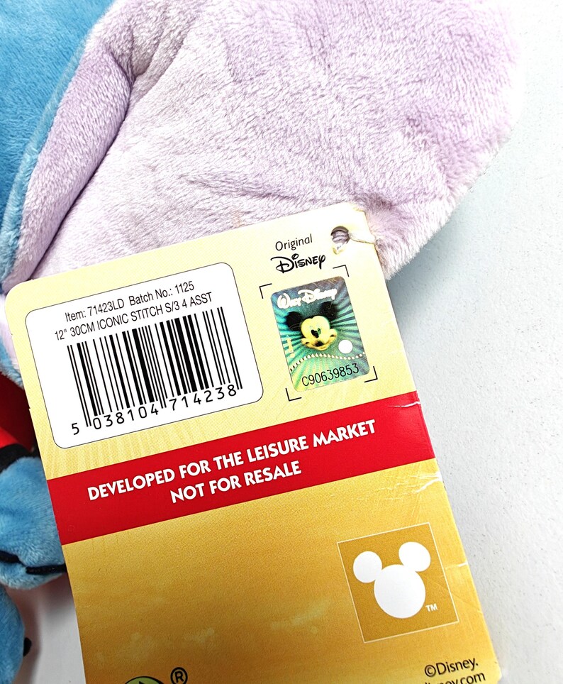 May include: A plush blue and purple Stitch toy with a Disney tag. The tag includes the text "12" 30CM ICONIC STITCH S/3 4 ASST" and "DEVELOPED FOR THE LEISURE MARKET NOT FOR RESALE". The tag also features the Disney logo.