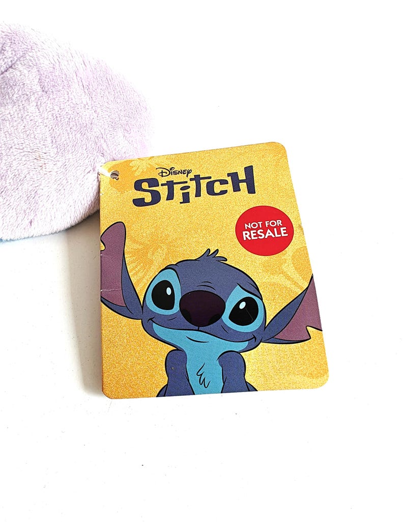 May include: A yellow tag featuring the Disney character Stitch with the word "Stitch" in blue and the text "NOT FOR RESALE" in a red circle. The tag has a cartoon image of Stitch.