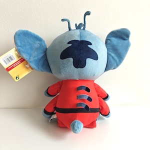 May include: A plush toy of the character Stitch from the Disney movie Lilo & Stitch. The toy has a blue head with large ears, a dark blue patch, and a red body with black accents. The toy is approximately 10 inches tall.