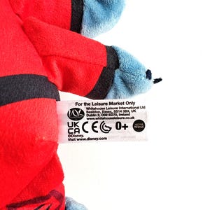 May include: A plush toy featuring red and blue colors. The toy has a red body with black accents and blue arms and feet. The tag reads "For the Leisure Market Only" and includes the Disney logo.
