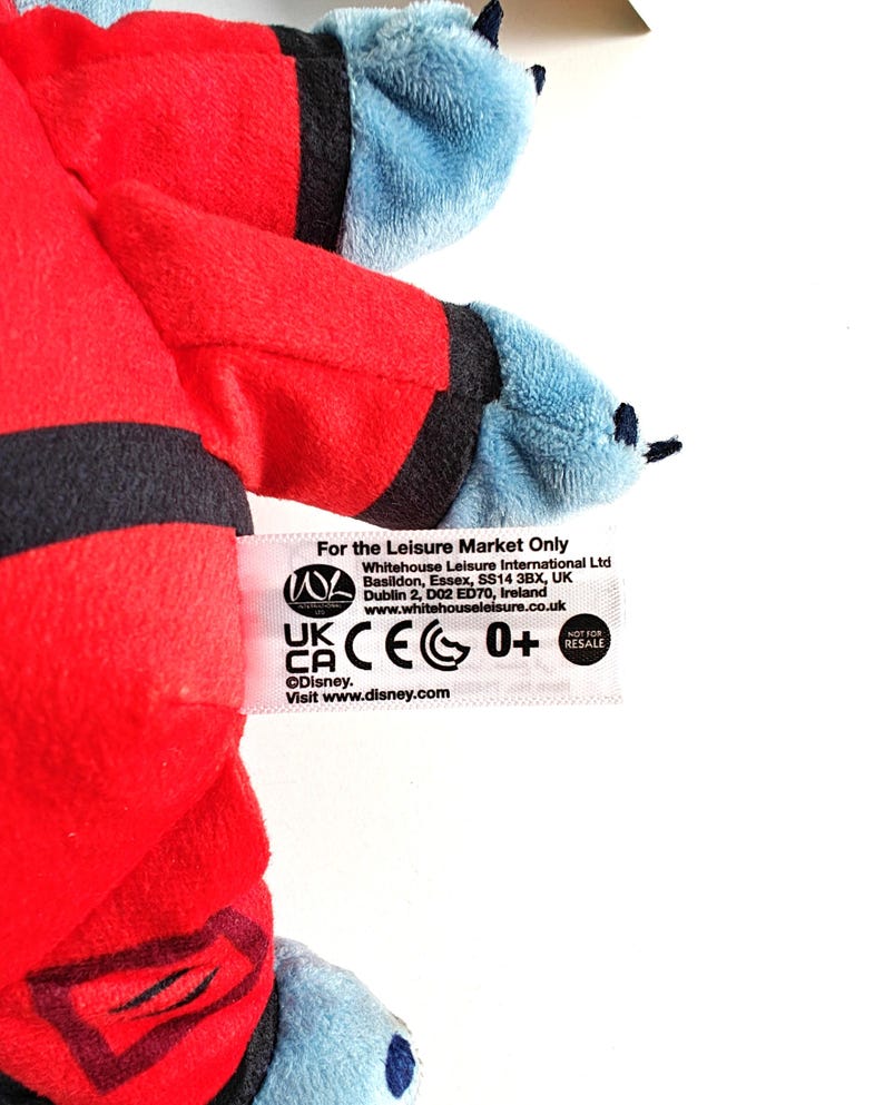 May include: A plush toy featuring red and blue colors. The toy has a red body with black accents and blue arms and feet. The tag reads "For the Leisure Market Only" and includes the Disney logo.