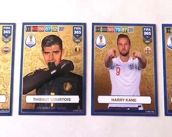 May include: Four trading cards featuring soccer players from the FIFA World Cup. The cards are blue and gold with the FIFA 365 logo. The players are Thibaut Courtois, Harry Kane, Kylian Mbappe, and a player wearing the Croatian jersey.