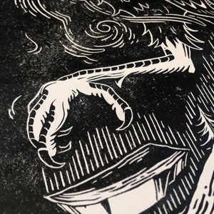 May include: Black and white linocut print of a bird's claw holding a box. The print has a textured, grainy look.