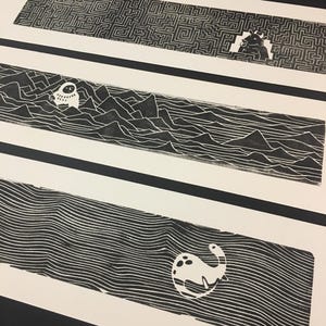 Peut inclure: Trois estampes en linoléum noir et blanc. La première estampe présente un motif de labyrinthe avec une créature à la fin. La deuxième estampe présente une créature dans un paysage montagneux. La troisième estampe présente une créature dans un motif ondulé.