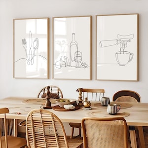 May include: Three framed line art prints. The first depicts a fork, knife, and spoon. The second shows a wine bottle, glass, cheese, and grapes. The third illustrates an espresso machine pouring into a cup. All are in black on a cream background.
