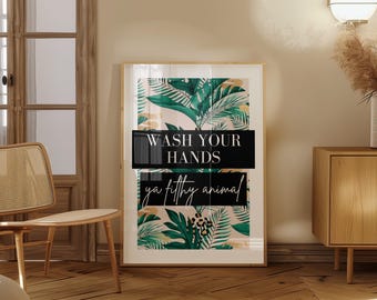 May include: A black and white framed print with a tropical leaf design. The print has the text "Wash your hands ya filthy animal" in white lettering.