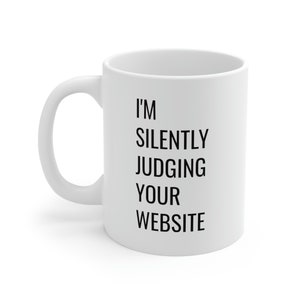 Peut inclure: Tasse à café en céramique blanche avec une anse incurvée. Le texte noir "I'M SILENTLY JUDGING YOUR WEBSITE" est imprimé sur le devant. Idéale pour les boissons chaudes ou froides.