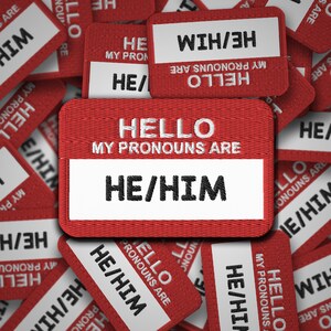 Könnte beinhalten: Rote Stoff-Namenskärtchen mit dem Text "Hallo, meine Pronomen sind" und den Pronomen "Er/Ihm".