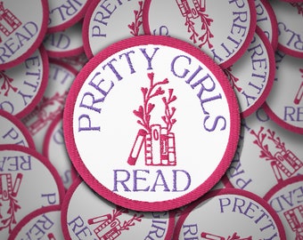 Puede incluir: Primer plano de varios parches de tela rosa y blanca con el texto "Pretty Girls Read" y una imagen estilizada de una pila de libros y una rama de flores.