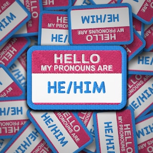 May include: A stack of pink and blue fabric patches with the text "Hello, my pronouns are" and the pronouns "He/Him" in white.