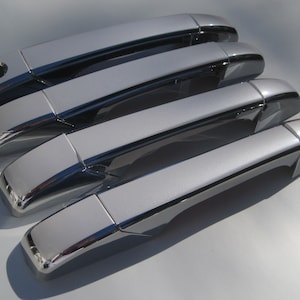 May include: Four silver car door handles with black accents. The handles are arranged in a row, with the top handle slightly offset from the others.