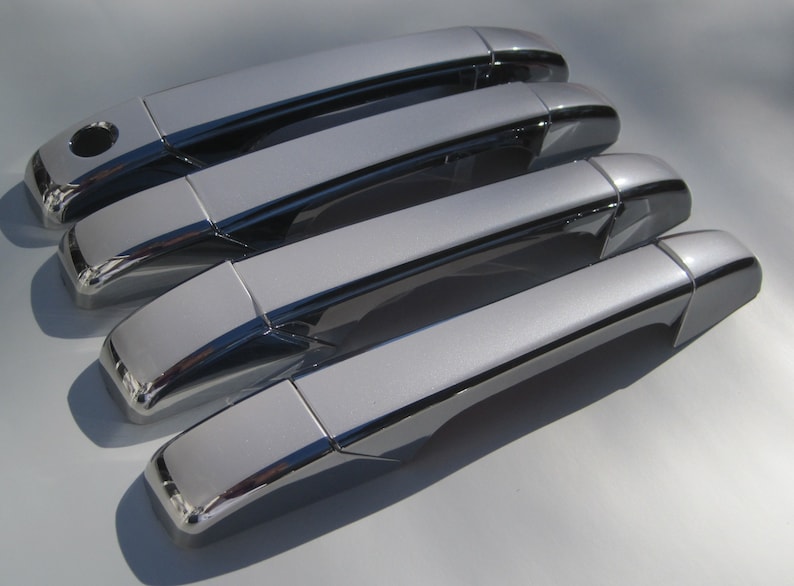 May include: Four silver car door handles with black accents. The handles are arranged in a row, with the top handle slightly offset from the others.