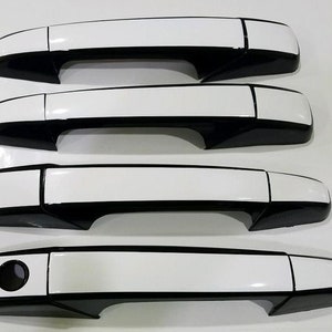 May include: Set of four black and white car door handles. The handles have a white top and a black bottom.
