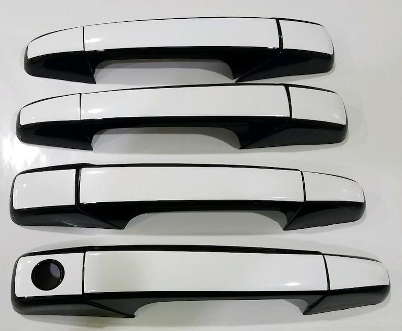 May include: Set of four black and white car door handles. The handles have a white top and a black bottom.
