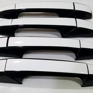 May include: Four black and white car door handles. The handles are made of plastic and have a glossy finish. The handles are designed to replace the original handles on a car.