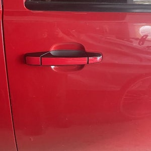 May include: A red car door with a black door handle. The handle has a red insert and a black trim.