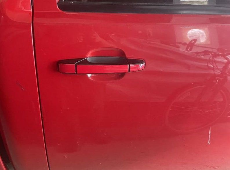 May include: A red car door with a black door handle. The handle has a red insert and a black trim.