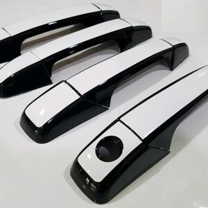 May include: Set of four black and white car door handles. The handles have a white top and a black bottom.