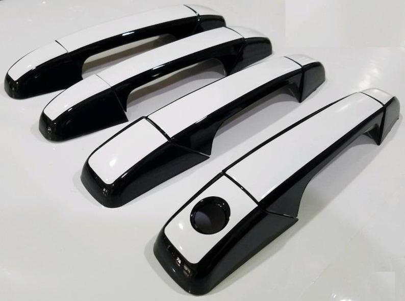 May include: Set of four black and white car door handles. The handles have a white top and a black bottom.