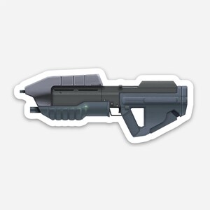 Könnte beinhalten: Ein futuristisches Gewehr in Grau und Schwarz mit einem grünen Licht an der Seite.