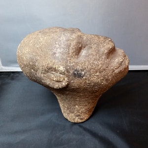 May include: A brown stone sculpture of a human head with closed eyes, tilted upwards. The sculpture is rough and textured, with a rounded shape.