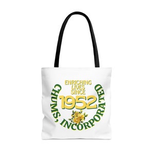 Peut inclure: Sac fourre-tout blanc avec un motif circulaire vert et jaune. Le cercle indique "Chums, Incorporated" et "Enriching Lives Since 1952". Il y a des fleurs jaunes au centre du cercle.