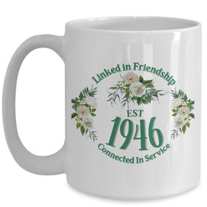 May include: White ceramic coffee mug with a green design that says "Linked in Friendship Est 1946 Connected in Service" with white flowers around the text.