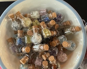 May include: A white ceramic bowl filled with small glass bottles containing various colored crystals and stones. The bottles have cork stoppers.