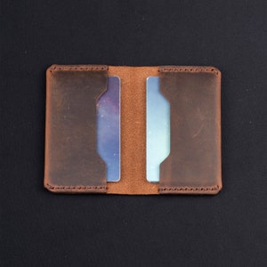 May include: A brown leather card holder with two slots for cards. The holder is open and the slots are empty.