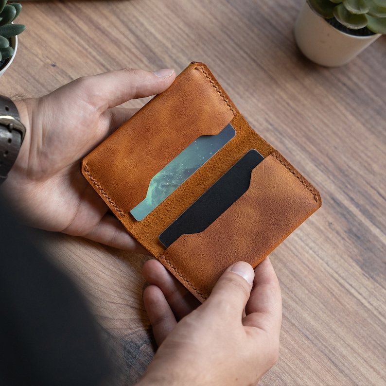 May include: A brown leather card holder with two slots for cards. The holder is open and the slots are visible.