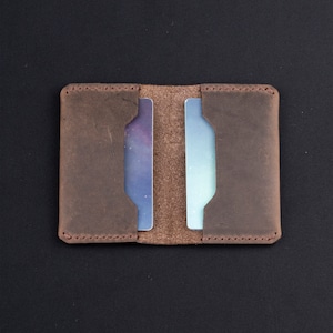 May include: A brown leather card holder with two slots for cards. The card holder is open and the slots are empty.