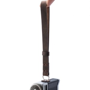 May include: A brown leather camera strap with a stitched design and an 'X' embossed on the strap.