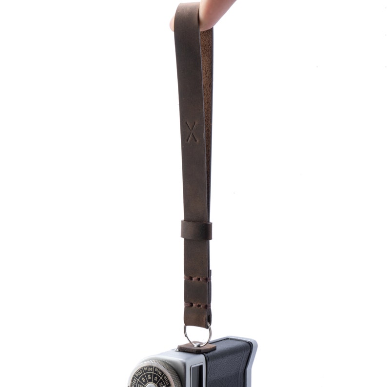 May include: A brown leather camera strap with a stitched design and an 'X' embossed on the strap.
