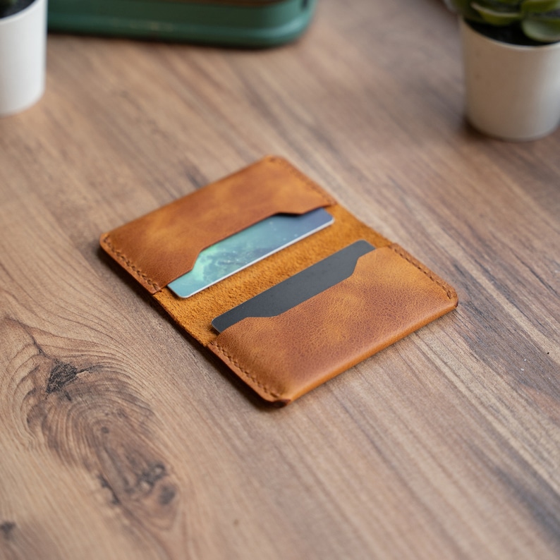 May include: A brown leather card holder with two cards inside. The card holder is on a wooden surface.