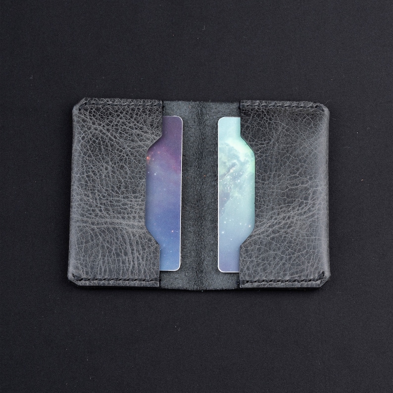 May include: A gray leather card holder with two slots for cards. The card holder is closed and the slots are empty.