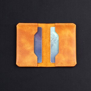 May include: A tan leather wallet with two card slots. The wallet is closed and has a stitched edge.