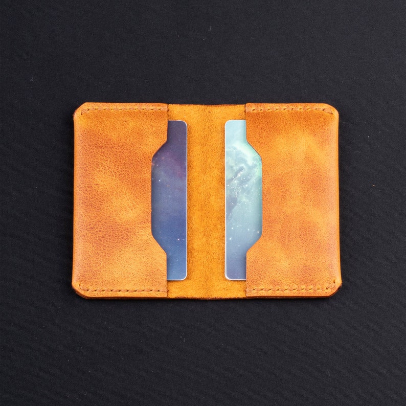 May include: A tan leather wallet with two card slots. The wallet is closed and has a stitched edge.