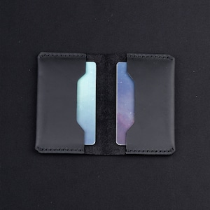 May include: A black leather card holder with two slots for cards. The card holder is closed and the slots are empty.
