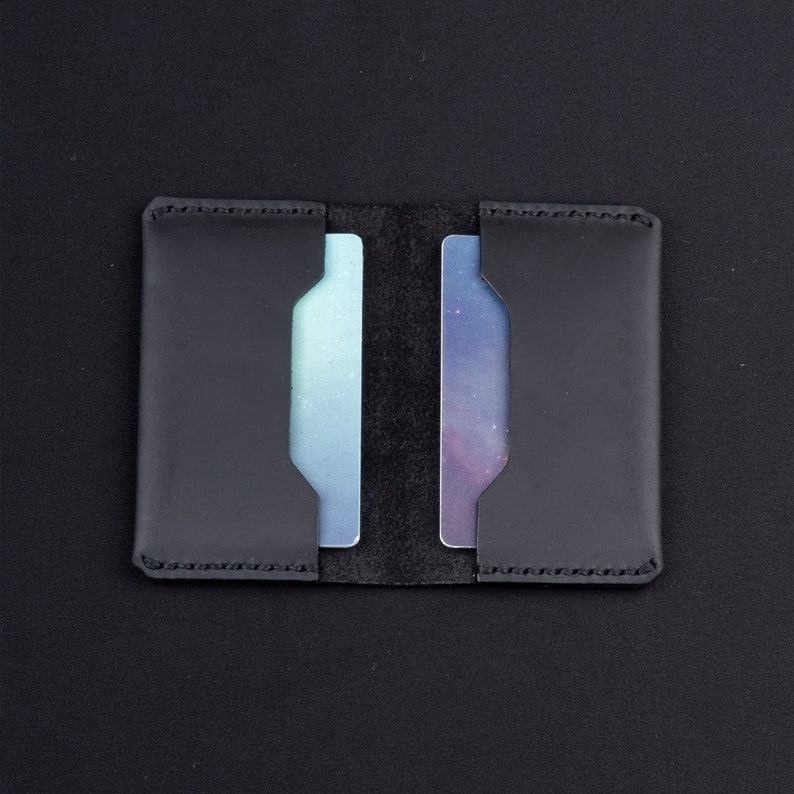 May include: A black leather card holder with two slots for cards. The card holder is closed and the slots are empty.
