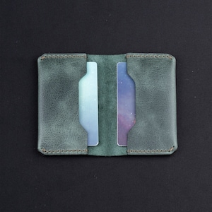 May include: A green leather card holder with two slots for cards. The holder has a distressed look and is stitched around the edges.