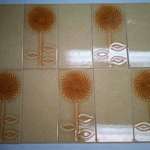 May include: Eight beige ceramic tiles featuring a raised design of a stylised flower with a brown centre. The flower has a spiral design and is surrounded by three leaves.