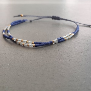 May include: Adjustable bracelet featuring a double strand design. The bracelet is made with small, dark blue beads and accented with gold and silver beads. The bracelet is tied with a dark blue cord.