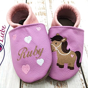 a pair of pink baby shoes with a horse on them