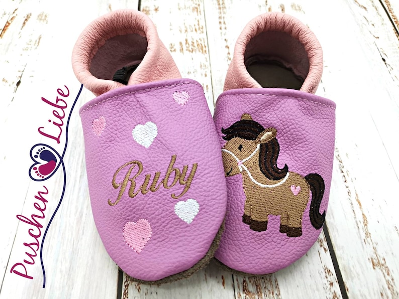 a pair of pink baby shoes with a horse on them