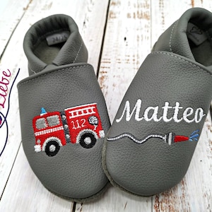 Könnte beinhalten: Graue Lederschuhe für Babys mit gesticktem Feuerwehrauto und Schlauch auf einem Schuh und dem Namen Matteo auf dem anderen.