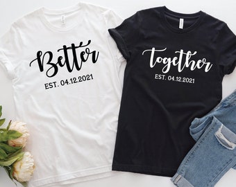 Peut inclure: Deux t-shirts blancs avec du texte noir. Un t-shirt dit "Better" et l'autre dit "Together". Les deux t-shirts ont la date "EST. 04.12.2021" imprimée sous le texte.