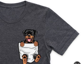 May include: A dark gray t-shirt with a pocket featuring a cartoon Rottweiler dog peeking out. The dog is brown and black with a white chest and a happy expression.