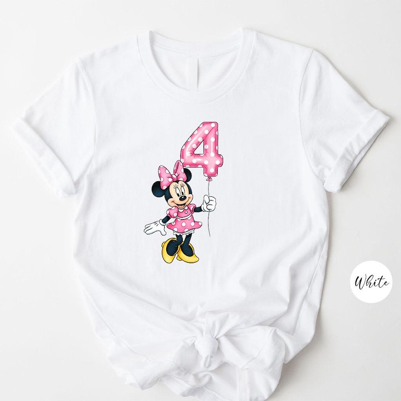 K&ouml;nnte beinhalten: Wei&szlig;es T-Shirt mit einer Cartoon-Minnie-Maus, die einen rosa Ballon mit der Zahl 4 h&auml;lt. Minnie Mouse tr&auml;gt ein rosa Kleid mit wei&szlig;en Punkten, eine passende Schleife und gelbe Schuhe. Das Design befindet sich mittig auf der Vorderseite des Shirts.