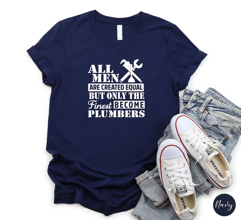 May include: Navy blue t-shirt with white text that reads "All men are created equal but only the finest become plumbers". The shirt features a white wrench and pipe graphic.