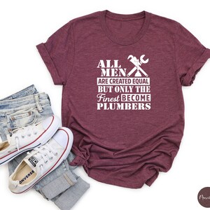 May include: A maroon t-shirt with white text that reads "All men are created equal but only the finest become plumbers". The text is accompanied by a graphic of crossed wrenches.